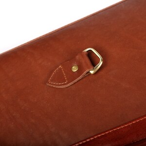 May include: A brown leather bag with a brass buckle and a flap closure.