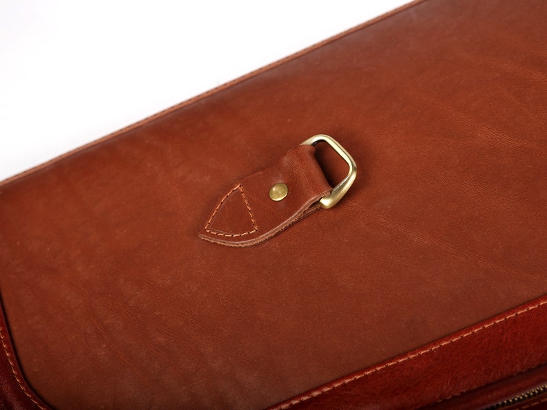 May include: A brown leather bag with a brass buckle and a flap closure.