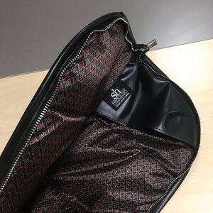 May include: Black leather zippered pouch with a red and black geometric patterned lining. The pouch has a label that reads "Steven Leather, Made in California".