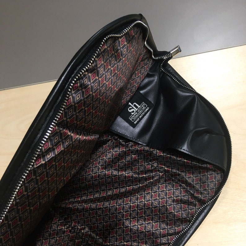 May include: Black leather zippered pouch with a red and black geometric patterned lining. The pouch has a label that reads "Steven Leather, Made in California".