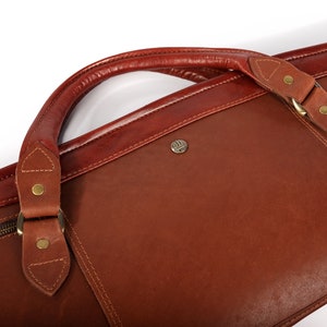 May include: A brown leather travel bag with a top handle and a zipper closure. The bag has a brass buckle and a brass logo on the front.