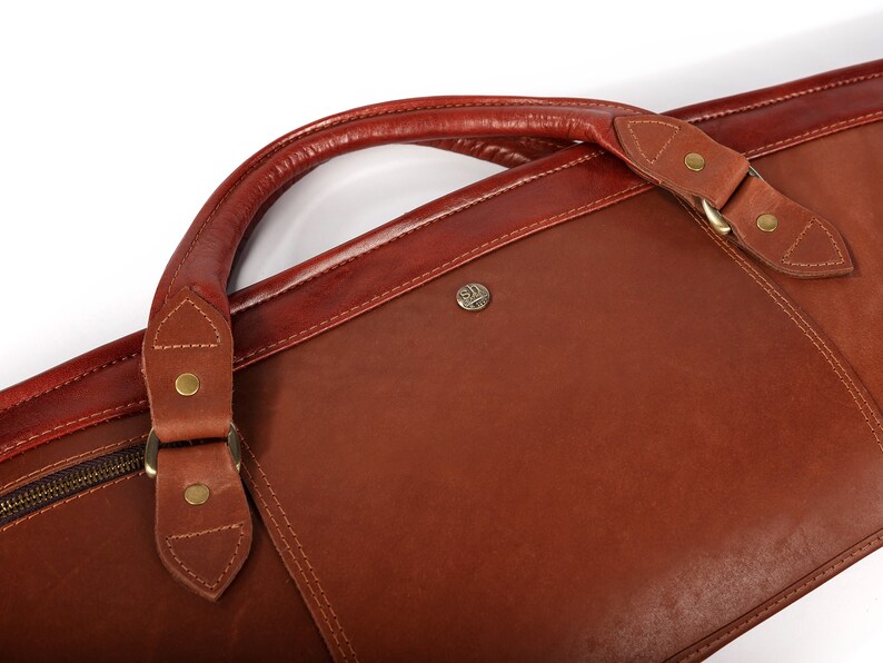 May include: A brown leather travel bag with a top handle and a zipper closure. The bag has a brass buckle and a brass logo on the front.