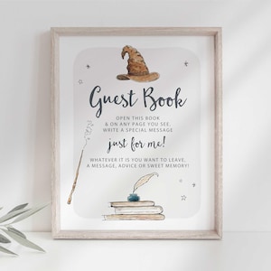 May include: A white sign with a black frame, featuring a watercolor illustration of a witch's hat, a wand, and a stack of books. The text reads "Guest Book, Open this book & on any page you see, write a special message just for me! Whatever it is you want to leave, a message, advice or sweet memory!"