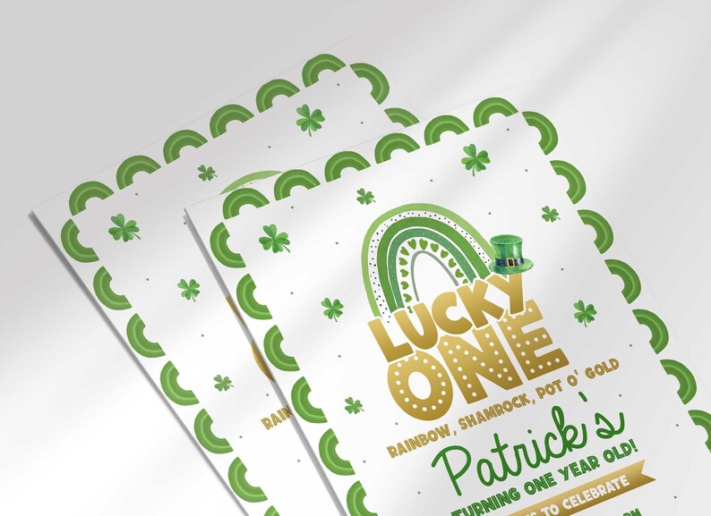 Styled close-up shot of two printed Lucky One St. Patrick's Day invitations stacked at an angle, green shamrock border and gold rainbow illustration, text reading Patrick's Turning One Year Old.