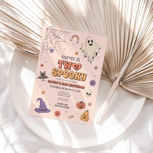 Lifestyle photo of Olivia's Halloween-themed birthday invitation propped on a white plate with a dried palm frond, styled on a linen tablecloth.