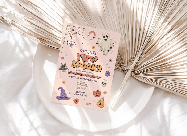 Lifestyle photo of Olivia's Halloween-themed birthday invitation propped on a white plate with a dried palm frond, styled on a linen tablecloth.