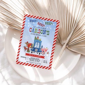 Carson's winter truck-themed birthday invitation displayed on a white plate with a dried palm frond, on a white linen background.