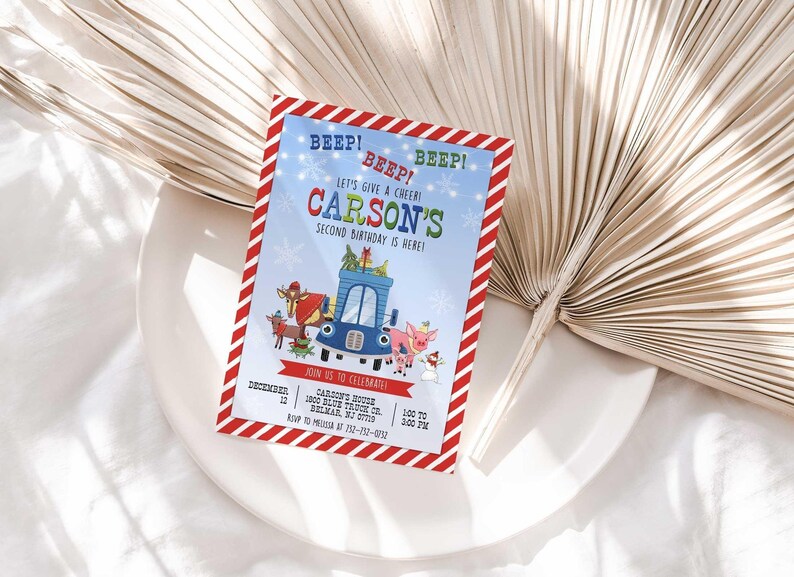 Carson's winter truck-themed birthday invitation displayed on a white plate with a dried palm frond, on a white linen background.