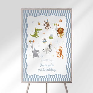 Puede incluir: Un letrero de cumpleaños enmarcado con un borde azul y blanco. El letrero presenta animales de dibujos animados como un león, una cebra y un cocodrilo. El texto dice "Bienvenido al 1er cumpleaños de Jaxson". El letrero está en un caballete de madera.