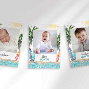 Three rectangular cards hang on a string, featuring a watercolor beach theme with surfboards, palm trees, ocean waves, and baby photos labeled newborn, three months, and twelve months.