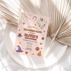 Lifestyle photo of Olivia's Halloween-themed birthday invitation propped on a white plate with a dried palm frond, styled on a linen tablecloth.