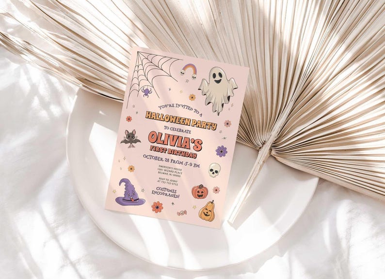Lifestyle photo of Olivia's Halloween-themed birthday invitation propped on a white plate with a dried palm frond, styled on a linen tablecloth.