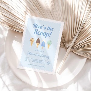 Styled lifestyle photo of the printed invitation propped on a white plate with a dried palm frond, showing the "Here's the Scoop!" ice cream design.