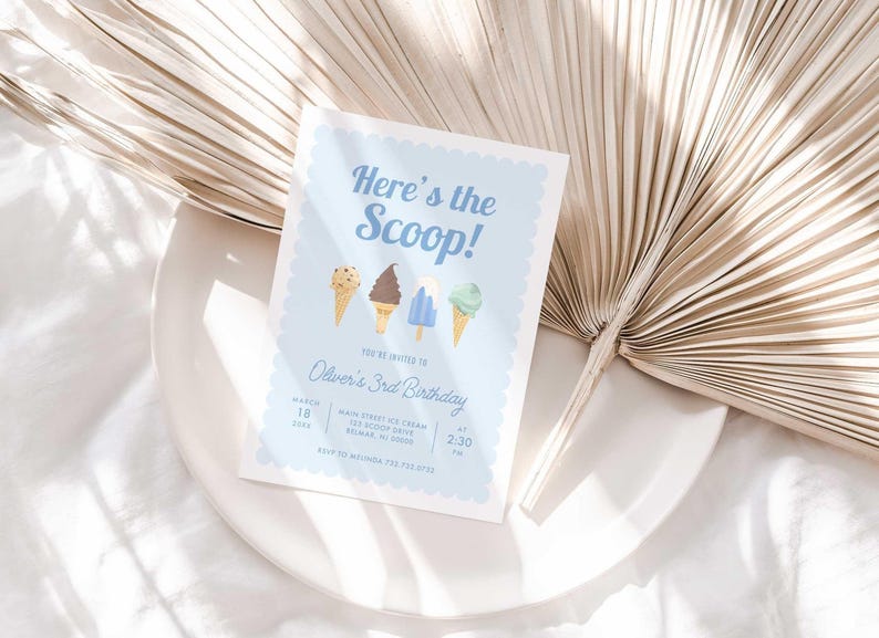 Styled lifestyle photo of the printed invitation propped on a white plate with a dried palm frond, showing the "Here's the Scoop!" ice cream design.