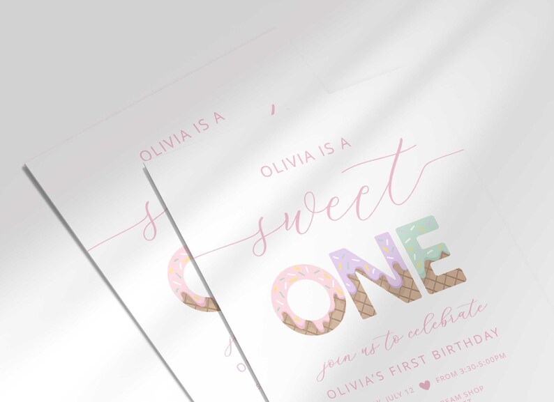 Angled close-up of two overlapping "Sweet ONE" invitations, highlighting the pastel confetti lettering and pink cursive script up close.