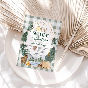 Lifestyle photo of Andrew and Lydia's camping-themed baby shower invitation propped on a white plate with a dried palm frond, styled on a linen tablecloth.
