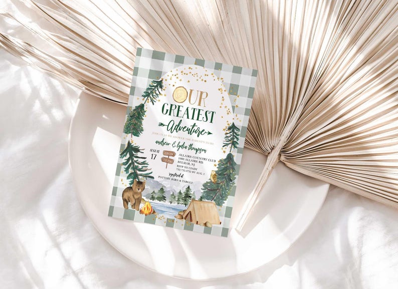 Lifestyle photo of Andrew and Lydia's camping-themed baby shower invitation propped on a white plate with a dried palm frond, styled on a linen tablecloth.