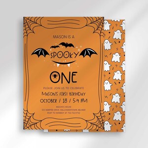 A Halloween-themed first birthday invitation on an orange background with a black spiderweb border and hand-drawn bat illustrations, reading 'Mason is a Spooky One, please join us to celebrate Mason's first birthday,' plus date, time, address, and RSVP details.