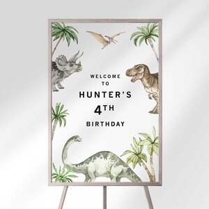 May include: A white welcome sign with a green, brown, and gray dinosaur illustration. The sign reads "Welcome to Hunter's 4th Birthday".