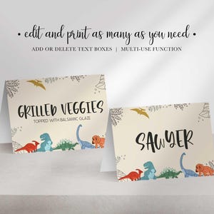 Two folded tent cards with dinosaur graphics display customized food labels reading GRILLED VEGGIES and SAWYER.