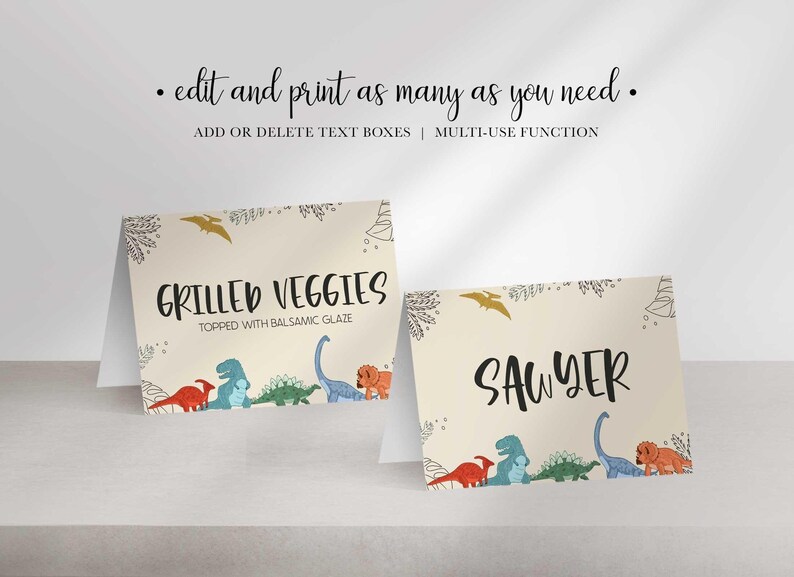 Two folded tent cards with dinosaur graphics display customized food labels reading GRILLED VEGGIES and SAWYER.