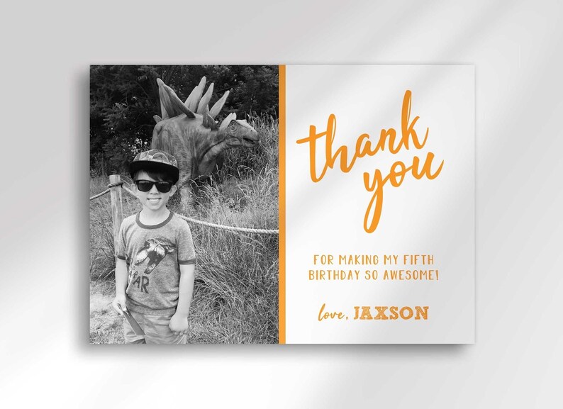 Full close-up view of the photo thank you card, showing a black-and-white photo of a boy wearing sunglasses and a cap at a dinosaur exhibit, and orange "thank you" text reading "for making my fifth birthday so awesome! love, Jaxson."