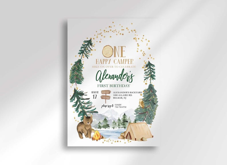 Camping-themed first birthday invitation with illustrated pine trees, a bear, a tent, and a campfire scene framed by a gold star arch, reading "One Happy Camper, hike on over to celebrate Alexander's first birthday" with the party date, time, and location.