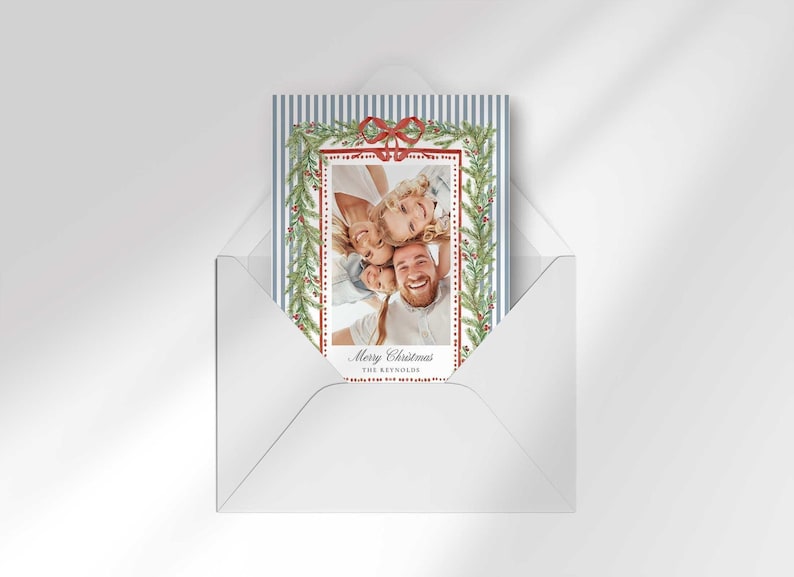A Christmas greeting card placed inside a white envelope on a neutral background.