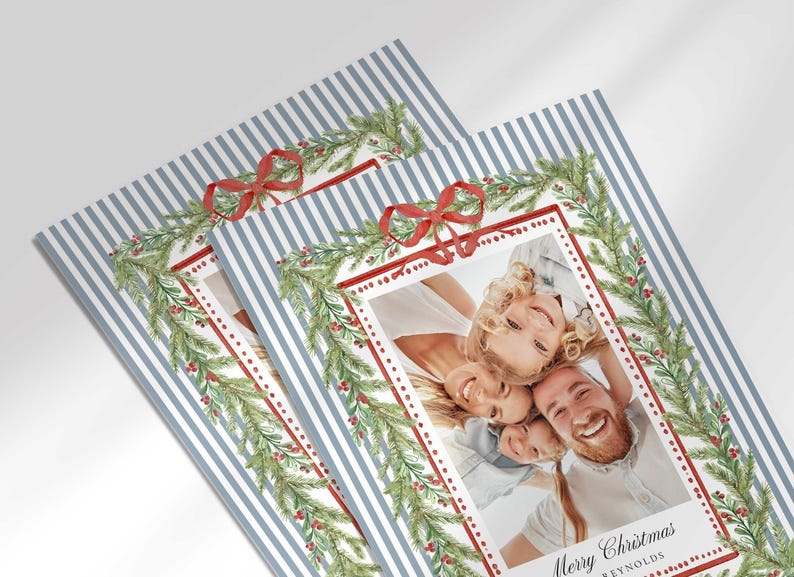 A close-up view of two overlapping Christmas greeting cards showing the detailed pine garland, red bow, and family portrait.