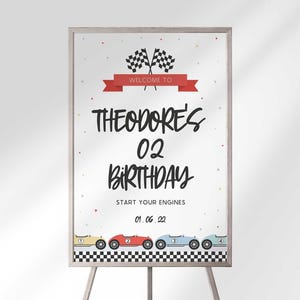 A framed race car birthday welcome sign on an easel displaying Theodore's 02 Birthday with checkered flags and vintage race cars.