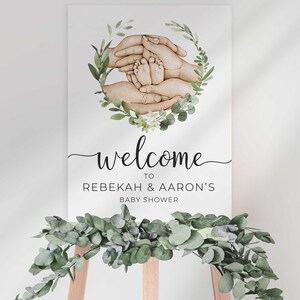 Welcome To Rebekah & Aaron's Baby Shower sign on an easel styled with a eucalyptus greenery garland draped along the bottom.