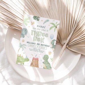 Lifestyle photo of William's dinosaur-themed birthday invitation propped on a white plate with a dried palm frond, styled on a linen tablecloth.