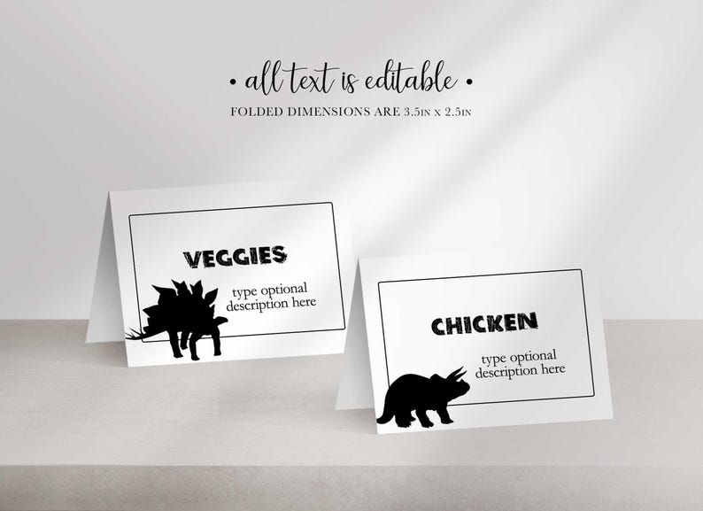 Two folded place cards stand side by side, one reading VEGGIES with a stegosaurus silhouette and the other CHICKEN with a triceratops silhouette.