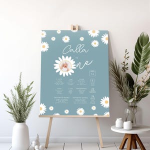 Lifestyle room mockup of the "Calla Is One" poster displayed on a wooden easel in a bright, neutral-toned room with potted plants and a small side table.