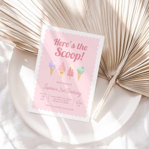 Styled lifestyle photo of the printed invitation propped on a white plate with a dried palm frond, showing the "Here's the Scoop!" ice cream design.