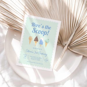 Styled lifestyle photo of the mint green ice cream invitation propped on a white plate against a gold dried palm frond, on a white linen surface.