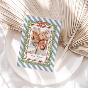 A Christmas greeting card resting on a white plate next to large decorative dried palm leaves.