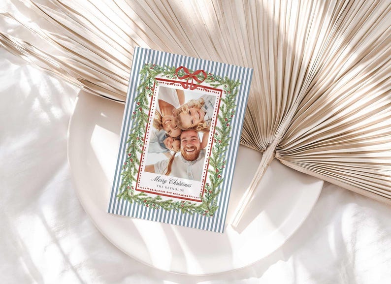 A Christmas greeting card resting on a white plate next to large decorative dried palm leaves.