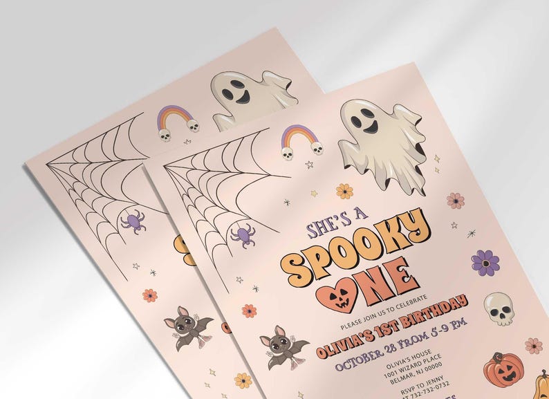 An angled close-up view of two of Olivia's Halloween-themed 'She's a Spooky One' first birthday invitations with illustrated ghosts, bats, and a spiderweb.