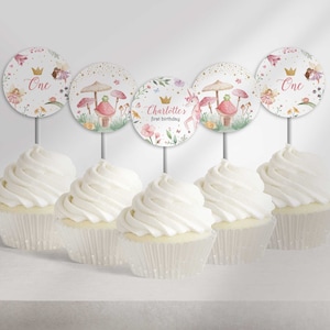 Op de afbeelding: Zes cupcakes met witte frosting, bedekt met ronde, kleurrijke cupcake-toppers met een eenhoorn, paddenstoelen en de woorden "One" en "Charlotte's first birthday".