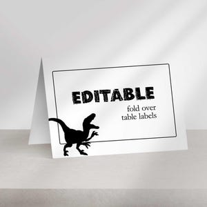 A blank folded place card stands on a surface featuring a black silhouette of a raptor and the text EDITABLE fold over table labels.