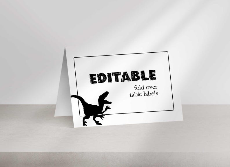 A blank folded place card stands on a surface featuring a black silhouette of a raptor and the text EDITABLE fold over table labels.