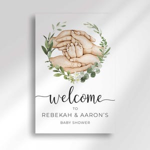 Close-up flat view of the printed Welcome To Rebekah & Aaron's Baby Shower sign with the watercolor hands and greenery wreath.