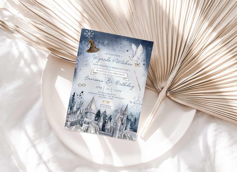 Lifestyle photo of the wintery wizard-themed birthday invitation resting on a white plate beside a dried palm frond, styled on a white linen tablecloth.