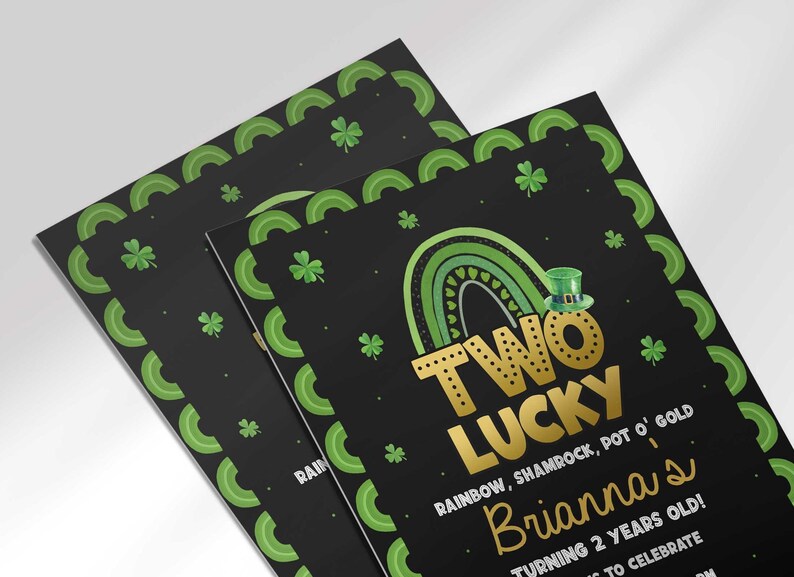 Close-up angled view of the printed Two Lucky birthday invitation showing the shamrock border and gold rainbow design detail.