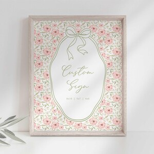 May include: A framed print with a floral design featuring pink flowers and green leaves. The print has a white oval in the center with a green ribbon and the text "Custom Sign" in cursive. The text "8x10 | 5x7 | 4x6" is below the text "Custom Sign".