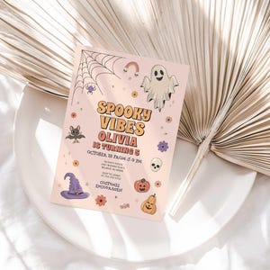 Lifestyle photo of the 'Spooky Vibes' Halloween birthday invitation resting on a white plate beside a dried palm frond, styled on a white linen tablecloth.