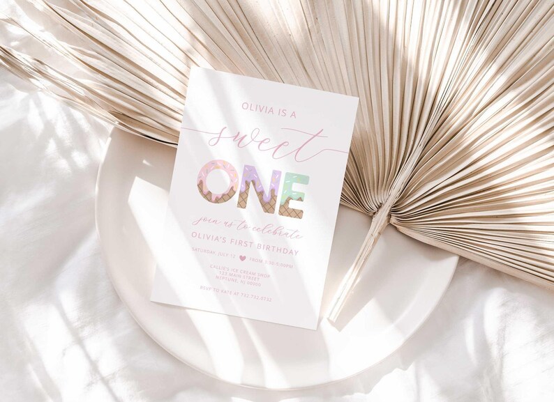Lifestyle styled shot of the "Sweet ONE" invitation resting on a white plate with a dried palm frond and soft white linen in the background.