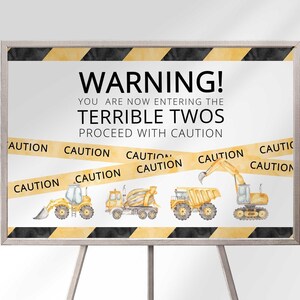 Construction warning tape themed Terrible Twos second birthday welcome sign printed on canvas in a black frame on an easel, with caution tape and construction vehicle illustrations.