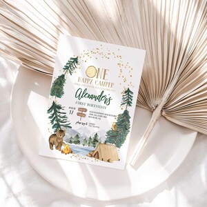 Lifestyle photo of Alexander's camping-themed birthday invitation propped on a white plate with a dried palm frond, styled on a linen tablecloth.